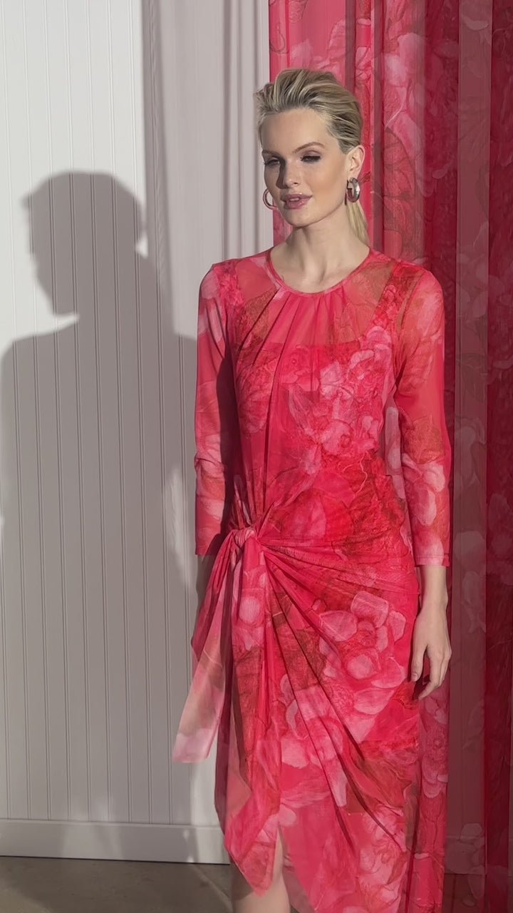 Woman wearing a sheer mesh wrap dress over a matching mini dress and as a bathing suit cover up in a red floral print by designer Ala von Auersperg for women's luxury travel clothing