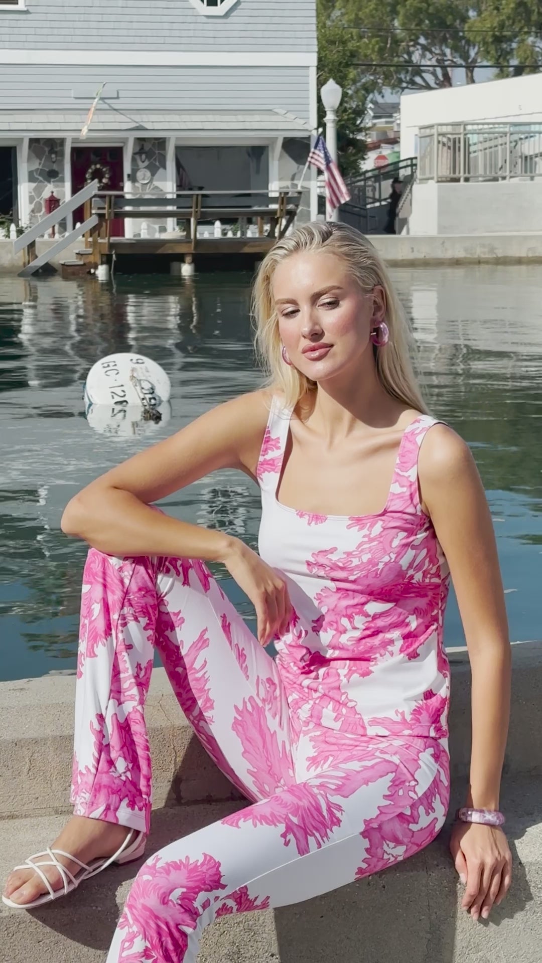 Woman wearing matching tank top and pants in a pink and white coral print by the water