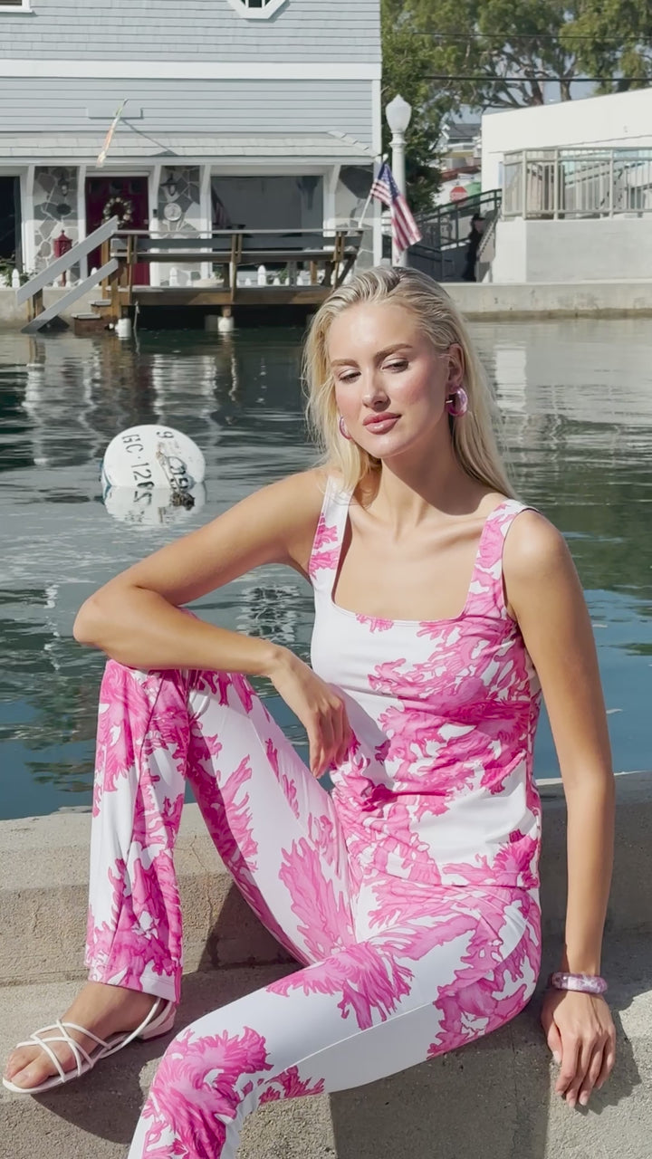 Woman wearing matching tank top and pants in a pink and white coral print by the water