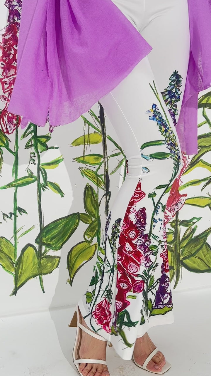 Video of a woman wearing white floral printed stretch knit pants with a white italian stretch cotton tank top and purple cashmere wrap by designer Ala von Auersperg for womens luxury travel clothing