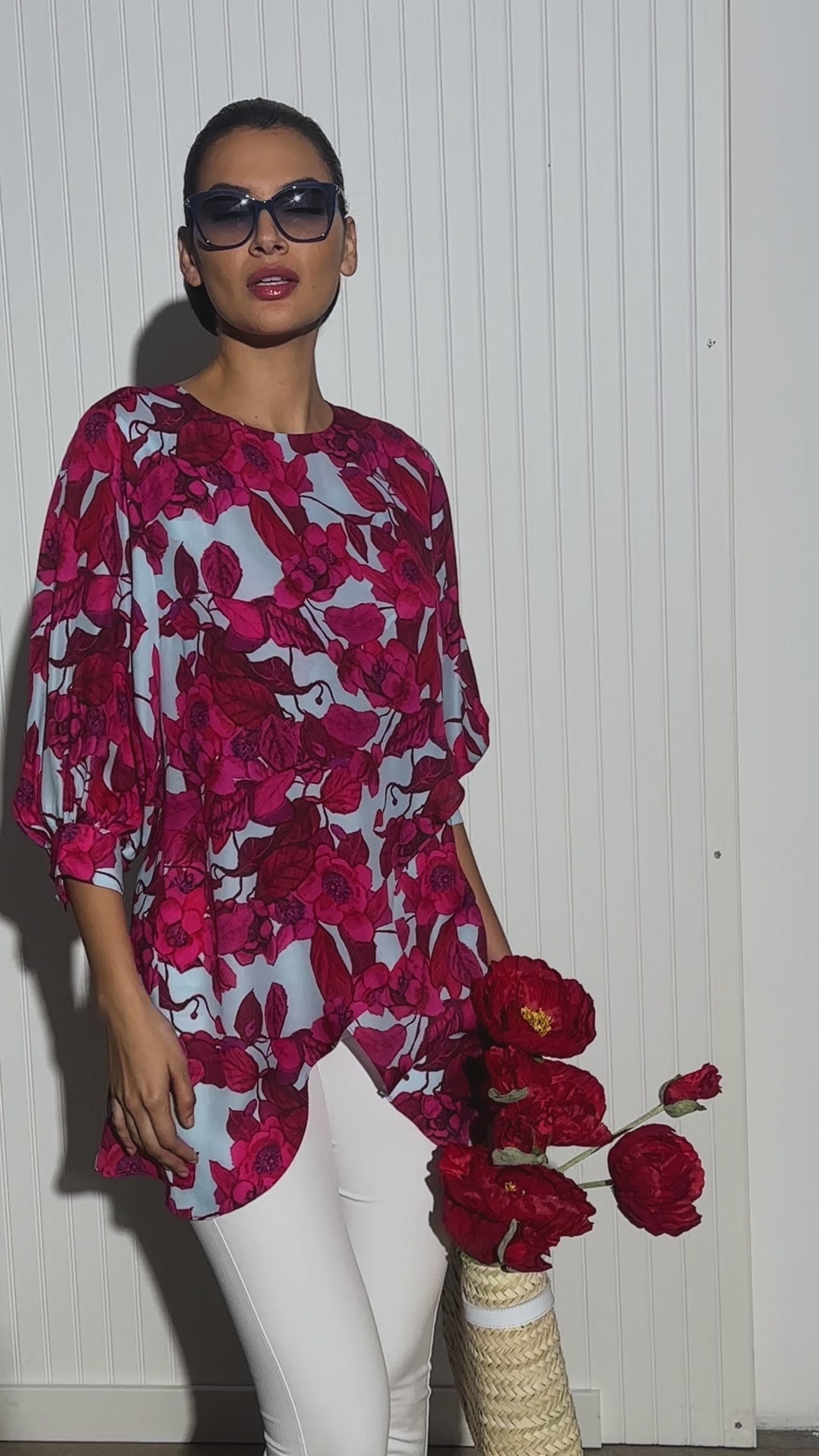 Video of a woman wearing a red floral printed silk blue with a blue background paired with white italian stretch cotton pants and a straw bag by designer Ala von Auersperg for womens luxury travel clothing