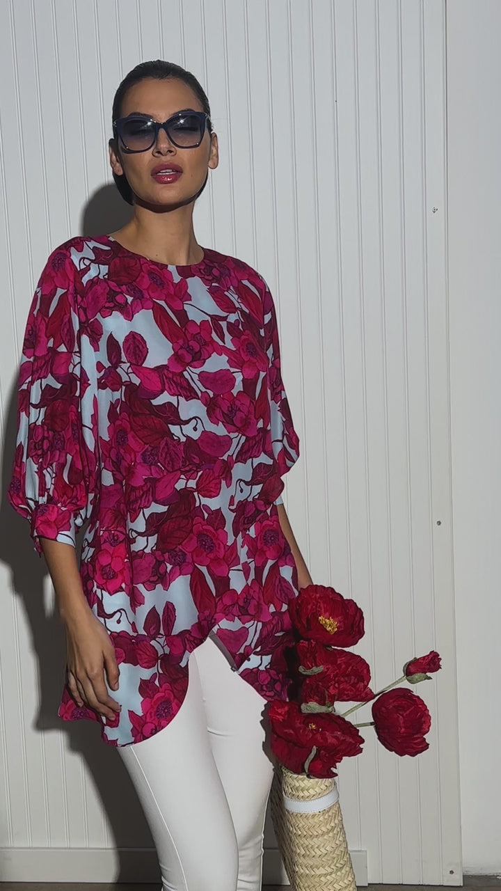 Video of a woman wearing a red floral printed silk blue with a blue background paired with white italian stretch cotton pants and a straw bag by designer Ala von Auersperg for womens luxury travel clothing