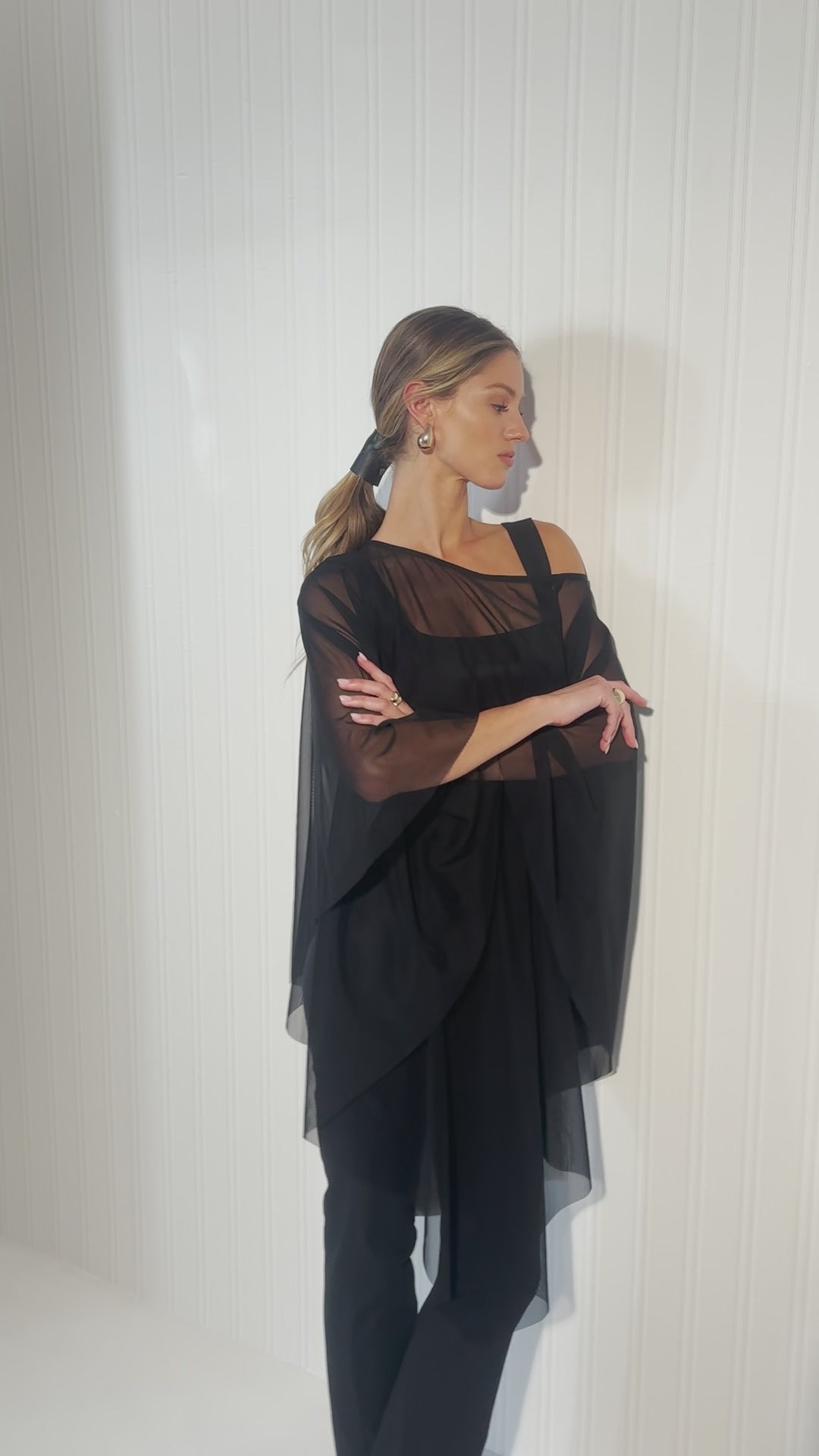 Video of a woman wearing a black mesh poncho over black tank top and pants by designer Ala von Auersperg for womens luxury travel clothing