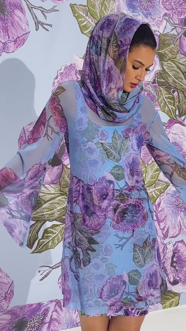 Video of a woman wearing a mesh hoodie over a matching mini dress and over a swimsuit as a cover up in a purple floral print by designer Ala von Auersperg for womens luxury travel clothing