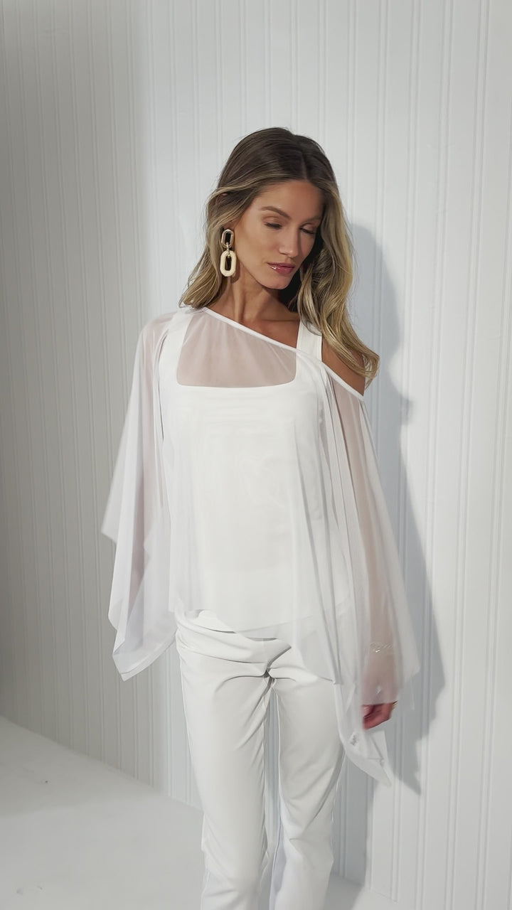 Video of a woman wearing a sheer mesh poncho over white cotton tank top and pants by designer Ala von Auersperg for womens luxury travel clothing