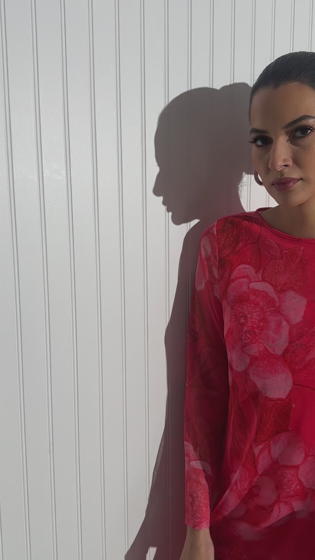 Woman wearing sheer top over a tank top and pants all in a red rose floral print by designer Ala von Auersperg for women's luxury travel clothing