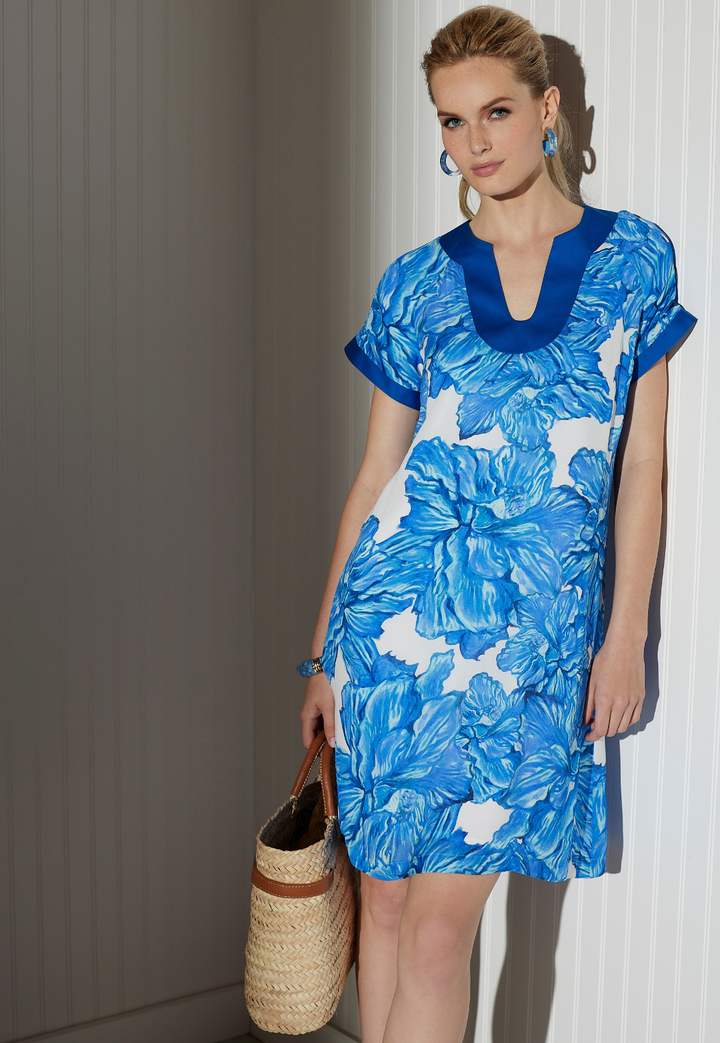 Woman wearing Shelly blue floral silk mini dress with royal blue trim, straw bag and blue coral earrings