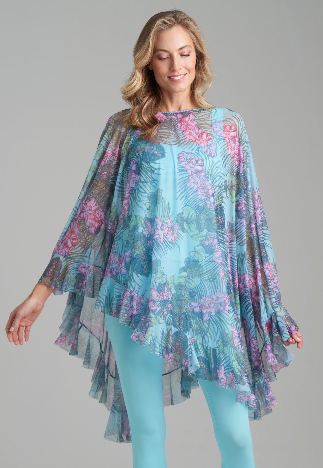 Woman wearing mesh printed orchid and palm poncho over stretch knit tank top and stretch knit pant in solid blue by Ala von Auersperg for resort 2022