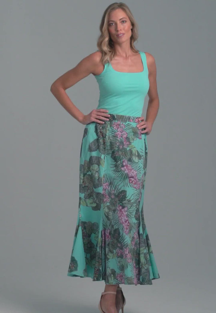 Woman wearing blue stretch knit square neck tank top with cotton grape leaf and orchid printed green cotton peasant skirt by Ala von Auersperg for resort 2022