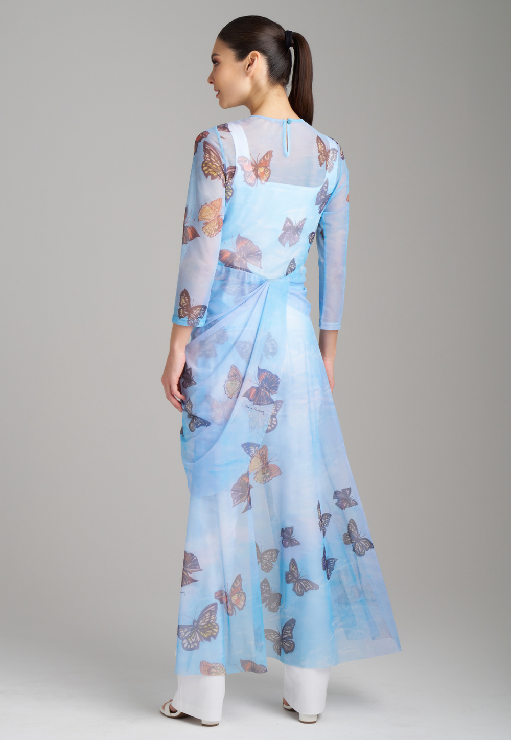 Woman wearing mesh blue butterfly printed asymmetrical topper over italian white stretch cotton tank top and pants by Ala von Auersperg for spring 2023