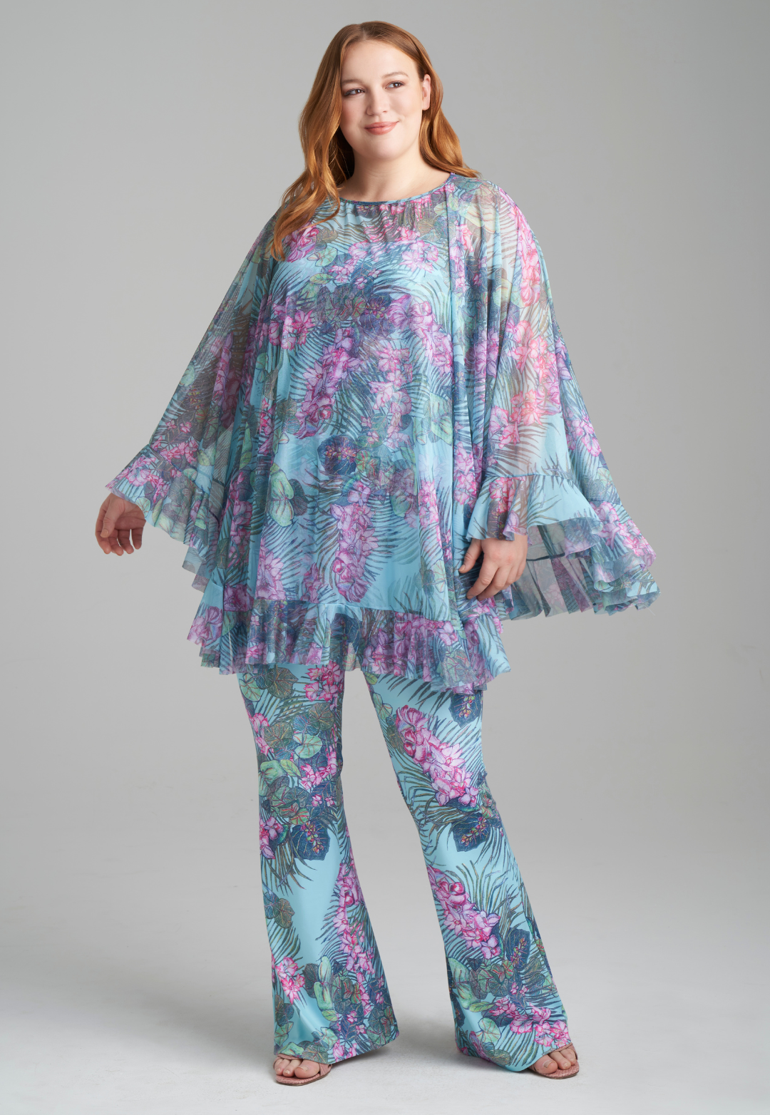 Woman wearing orchid and palm printed square neck stretch knit tank top and orchid and palm printed skinny leg pants with mesh printed poncho by Ala von Auersperg for resort 2022