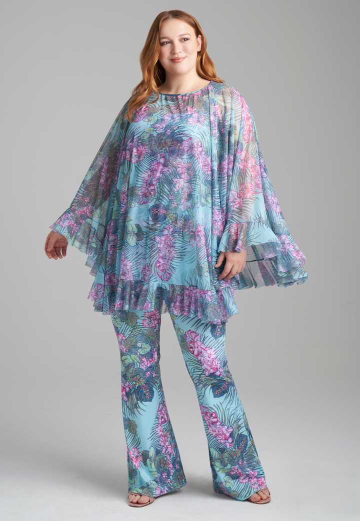 Woman wearing orchid and palm printed square neck stretch knit tank top and orchid and palm printed skinny leg pants with mesh printed poncho by Ala von Auersperg for resort 2022