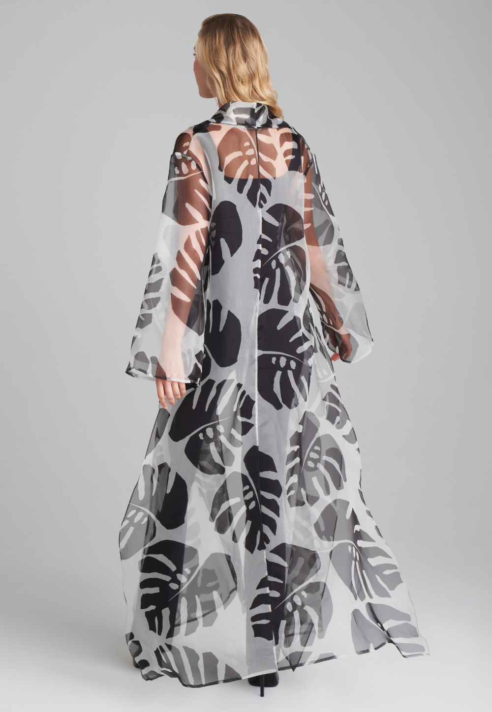Woman wearing silk black and white palm leaf printed printed organza long jacket duster over italian stretch cotton square neck tank top and pant in black by Ala von Auersperg for holiday 2022