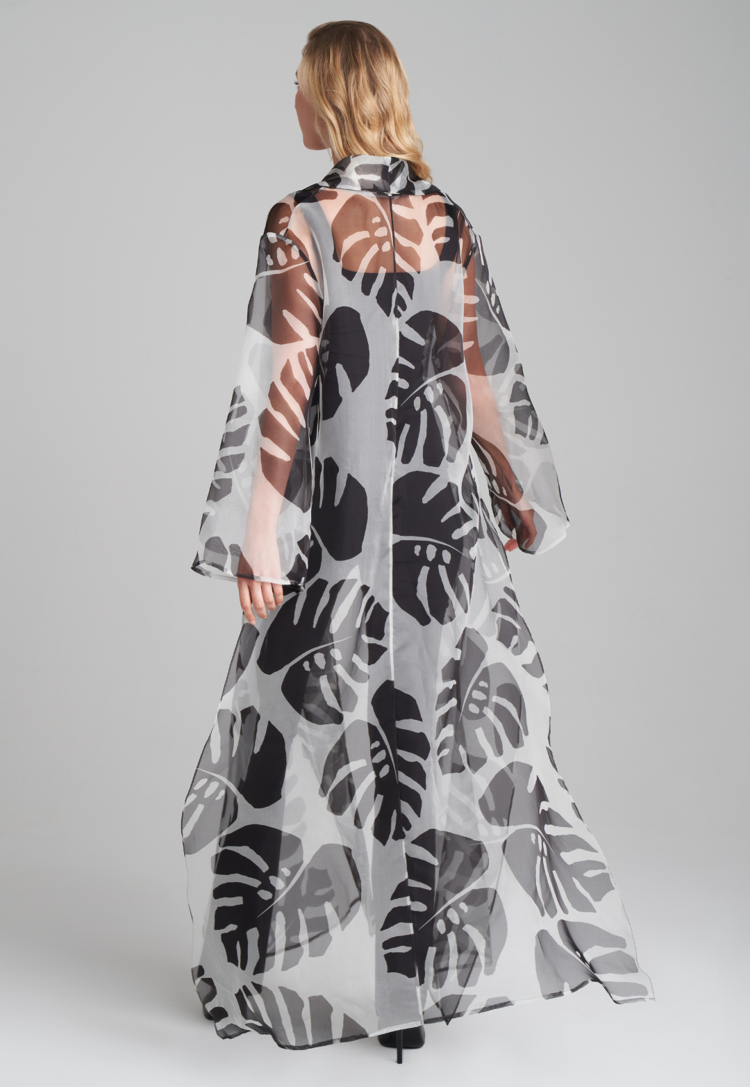 Woman wearing silk black and white palm leaf printed printed organza long jacket duster over italian stretch cotton square neck tank top and pant in black by Ala von Auersperg for holiday 2022