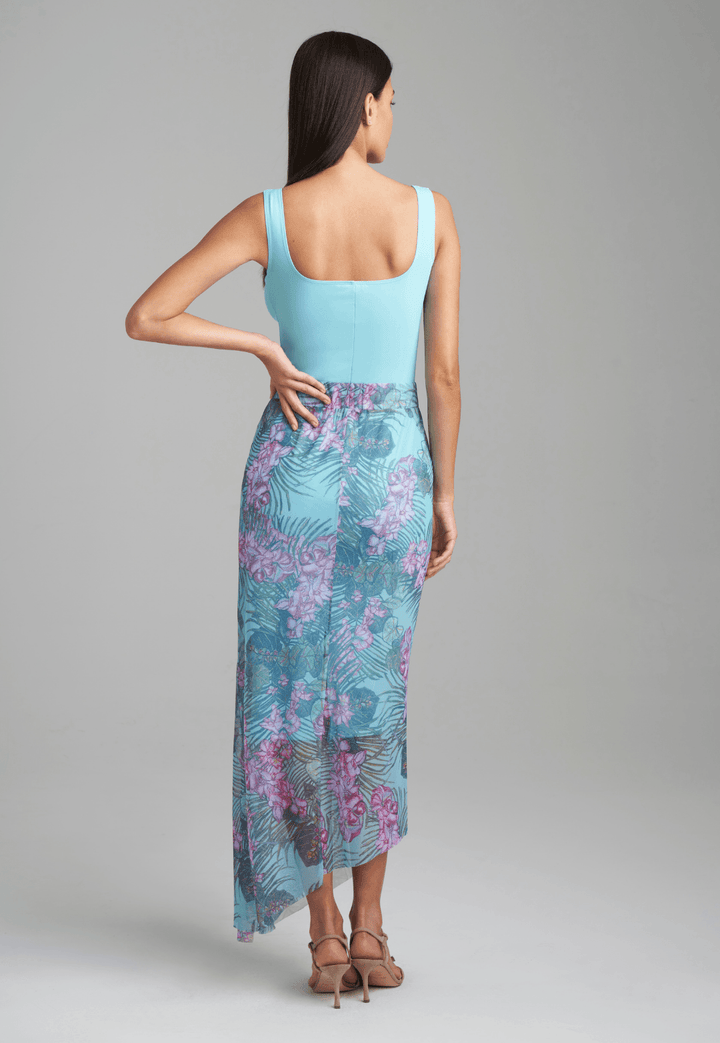 Woman wearing stretch knit tank top in blue with mesh printed orchid and palm green skirt by Ala von Auersperg for resort 2022
