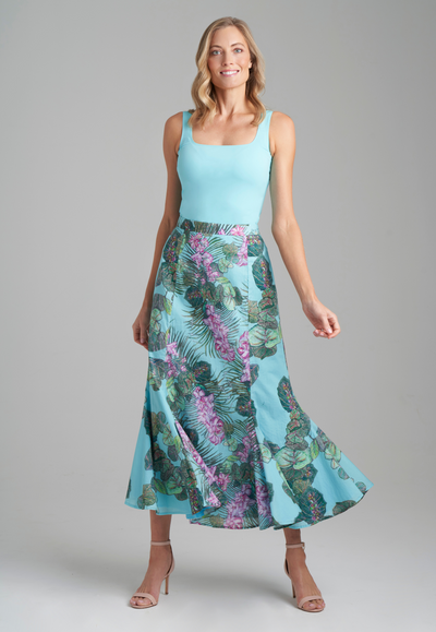 Woman wearing blue stretch knit square neck tank top with cotton grape leaf and orchid printed green cotton peasant skirt by Ala von Auersperg for resort 2022