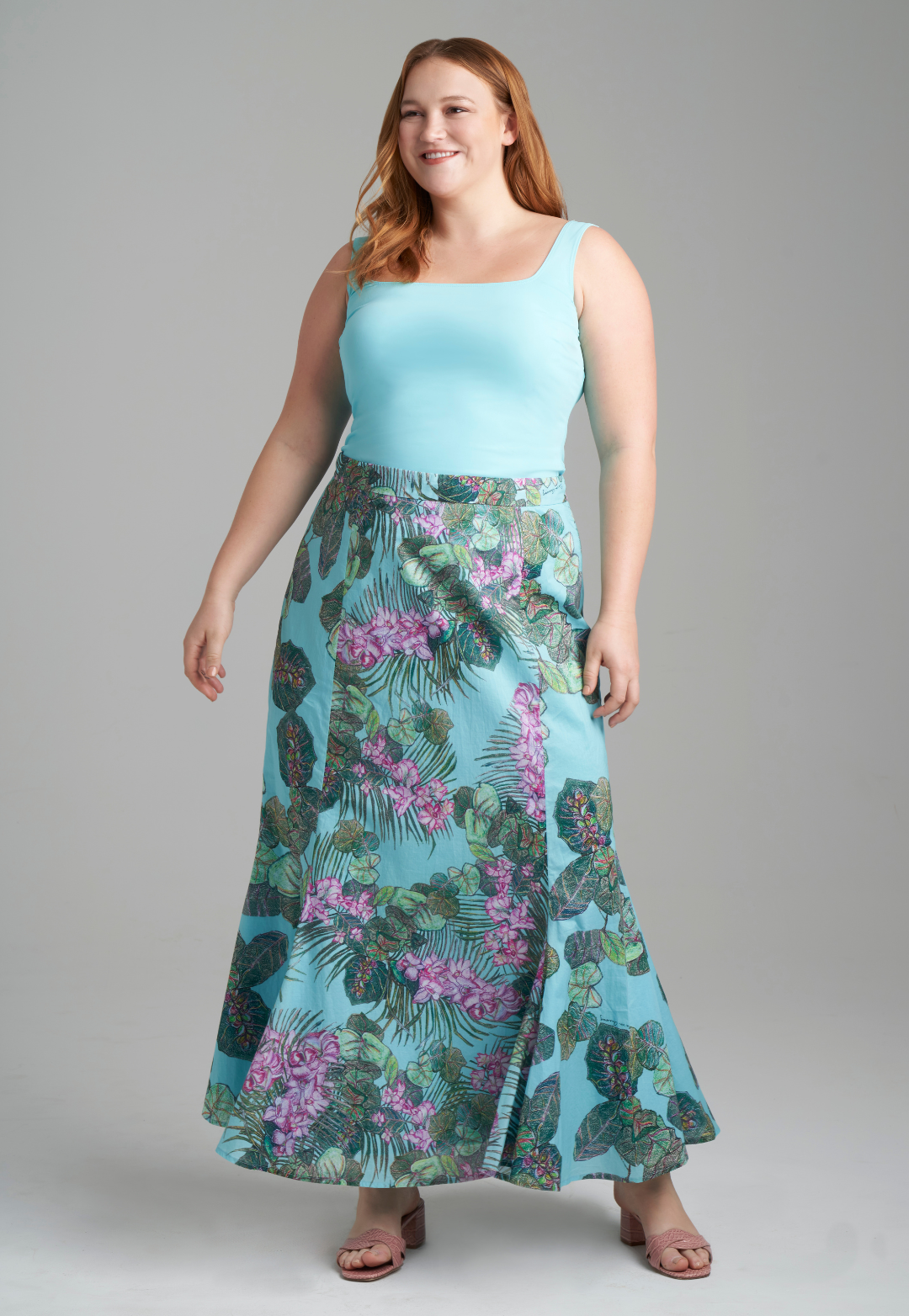 Woman wearing stretch knit solid blue green tank top with printed cotton orchid and palm and grape leaf skirt by Ala von Auersperg for resort 2022