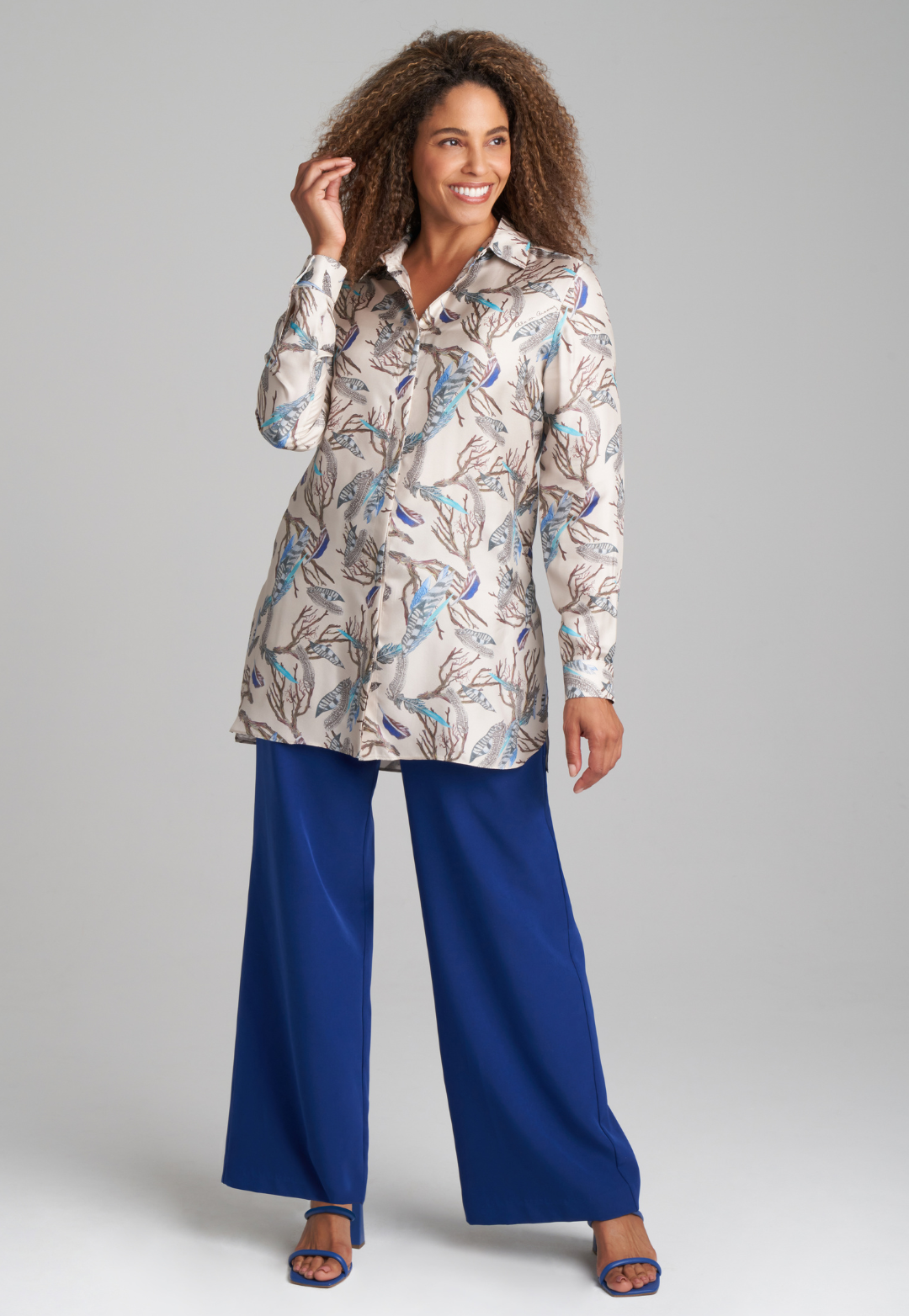 Woman wearing silk feather printed blouse and blue stretch knit pants by Ala von Auersperg for fall 2022