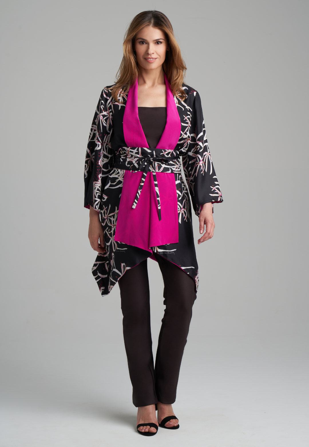Woman wearing silk black spider lily printed reversible pink robe jacket over black stretch knit tank top and pant by Ala von Auersperg