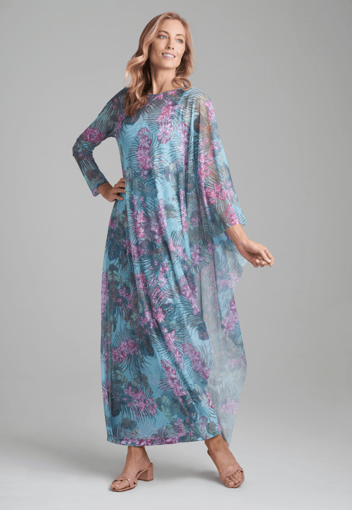 Woman wearing mesh long one sleeved poncho printed in orchid and palm over stretch knit long printed orchid and palm green  dress by Ala von Auersperg for resort 2022