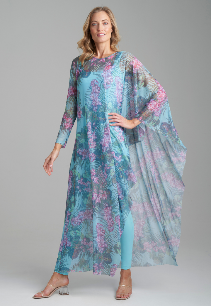 Woman wearing mesh long one sleeved poncho printed in orchid and palm over stretch knit tank top and skinny pant in blue by Ala von Auersperg for resort 2022