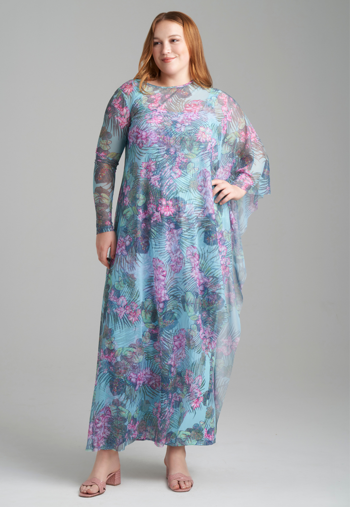 Woman wearing mesh long one sleeved poncho printed in orchid and palm over stretch knit long printed orchid and palm green dress by Ala von Auersperg for resort 2022