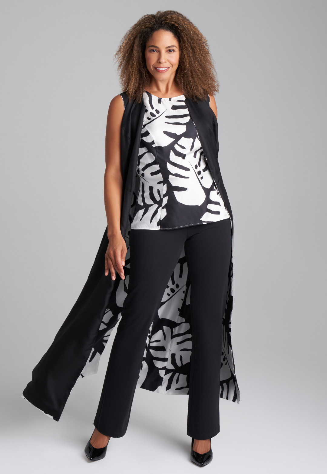 Woman wearing black and white palm leaf printed silk shell tank top with italian stretch cotton black pants  and reversible silk palm leaf black and white printed long vest by Ala von Auersperg for holiday 2022
