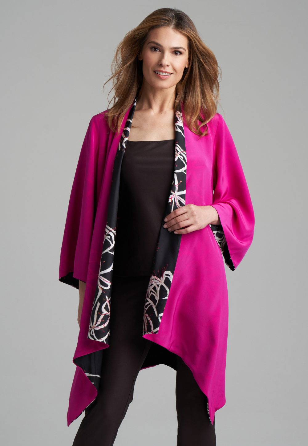 Woman wearing silk black spider lily printed reversible pink robe jacket over black stretch knit tank top and pant by Ala von Auersperg