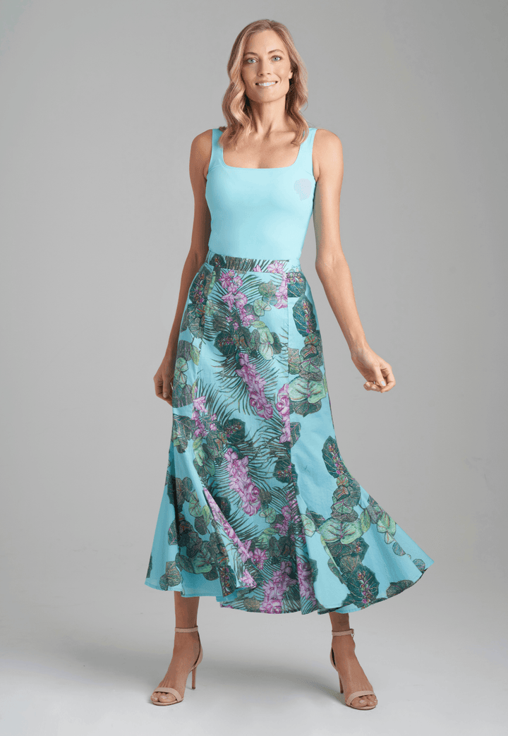 Woman wearing stretch knit solid blue green tank top with printed cotton orchid and palm and grape leaf skirt by Ala von Auersperg for resort 2022