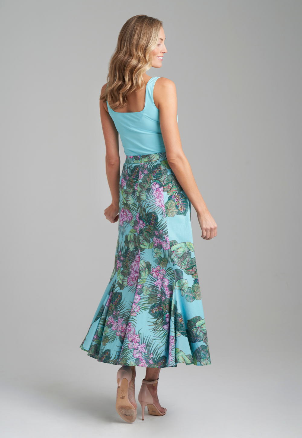 Woman wearing blue stretch knit square neck tank top with cotton grape leaf and orchid printed green cotton peasant skirt by Ala von Auersperg for resort 2022