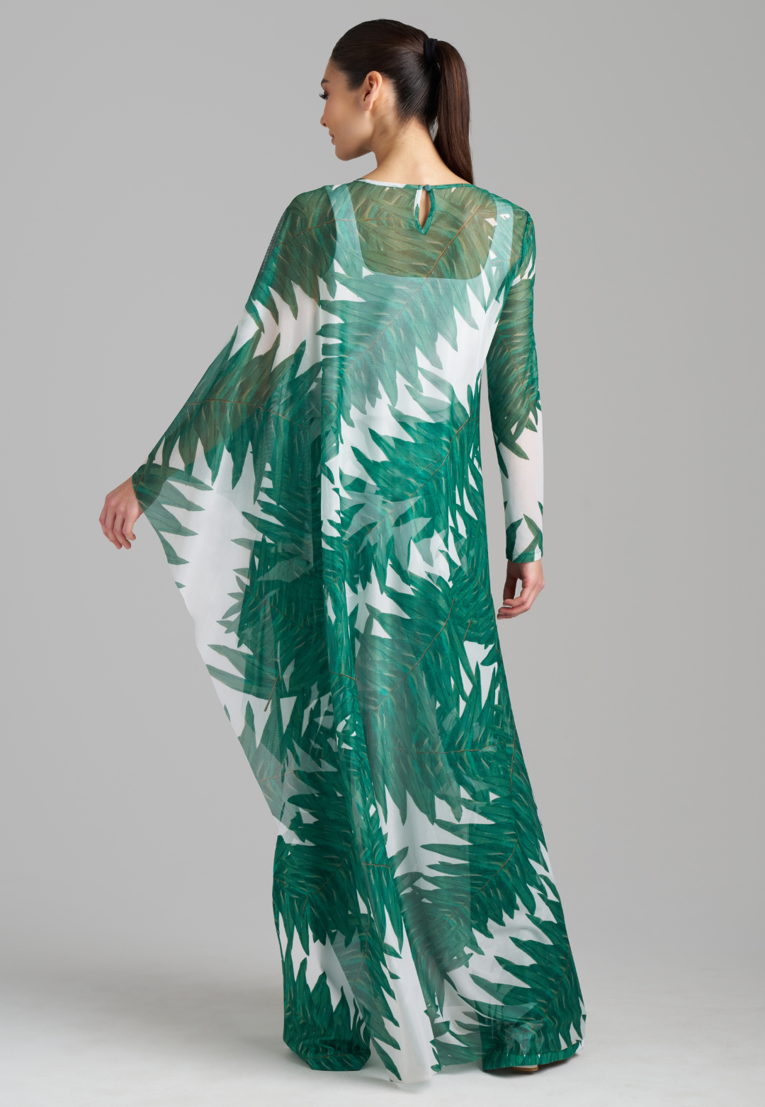 Woman wearing on armed mesh green palm leaf printed kaftan poncho over italian stretch cotton white tank top and green palm leaf printed stretch knit pants by Ala von Auersperg