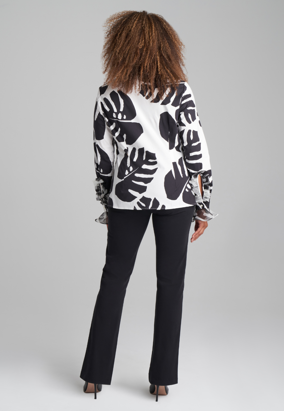 Woman wearing cotton turtleneck black and white palm leaf printed blouse with ruffle sleeve and collar details with italian stretch cotton pant in black by Ala von Auersperg for holiday 2022