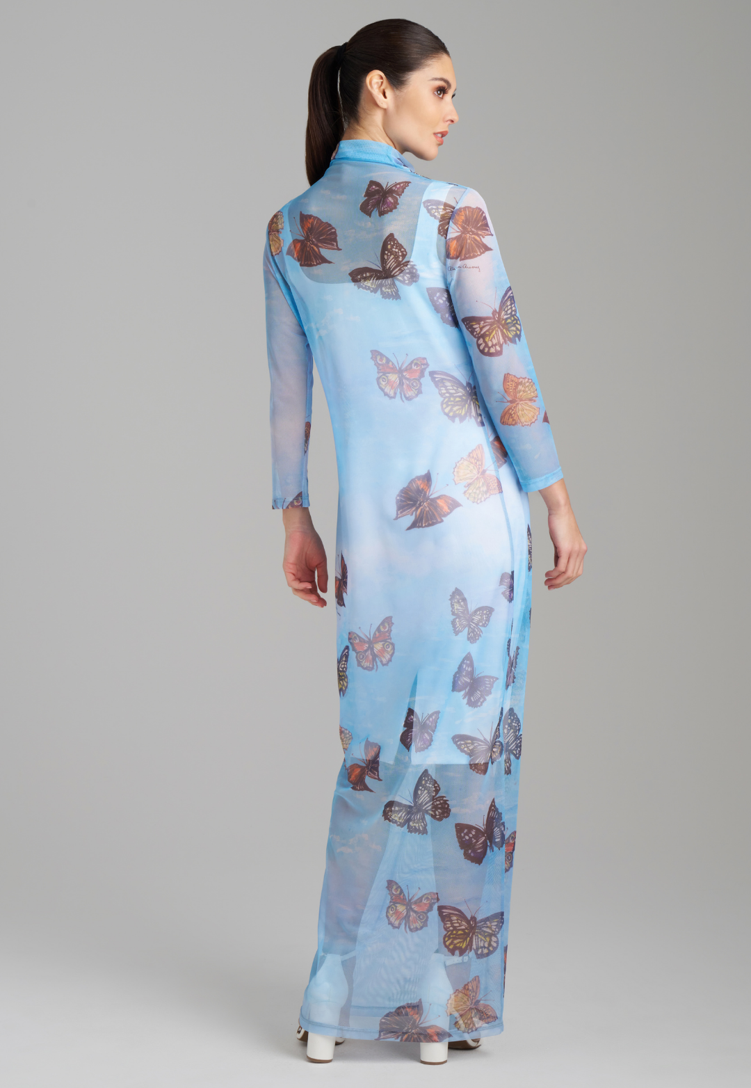 Woman wearing long mesh t shirt dress with turtleneck color in blue butterfly print over a short white stretch knit dress by Ala von Auersperg for spring 2023