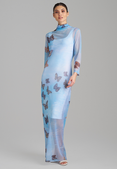 Woman wearing long mesh t shirt dress with turtleneck color in blue butterfly print over a short white stretch knit dress by Ala von Auersperg for spring 2023