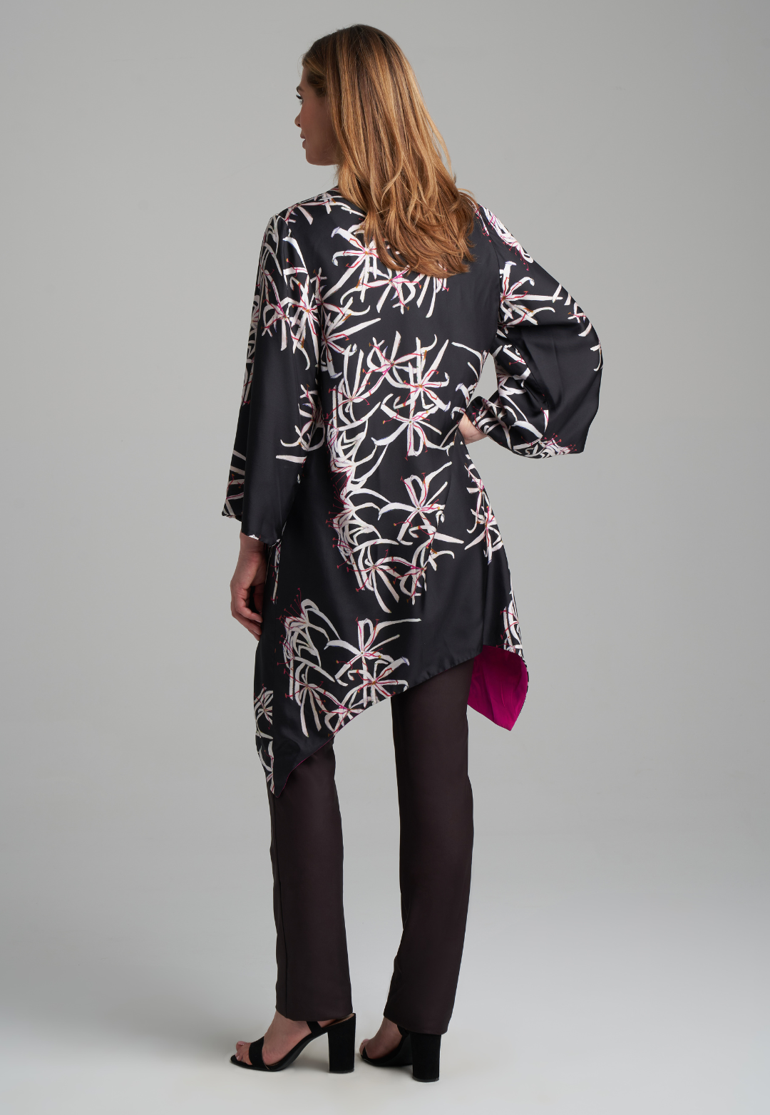 Woman wearing silk black spider lily printed reversible pink robe jacket over black stretch knit tank top and pant by Ala von Auersperg