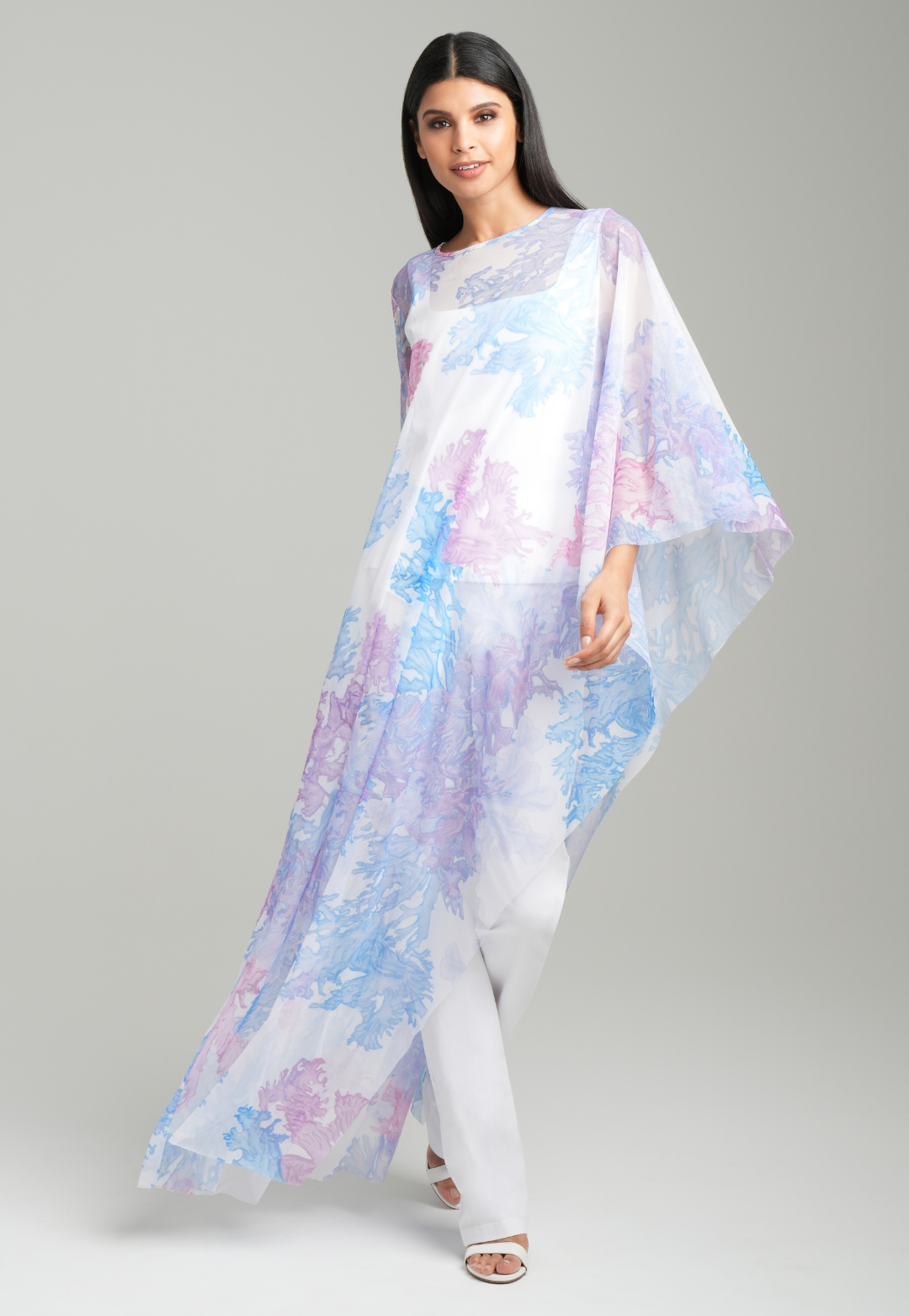 Woman wearing rainbow coral printed mesh one armed kaftan poncho over italian stretch cotton white tank top and pants by Ala von Auersperg for resort 2023