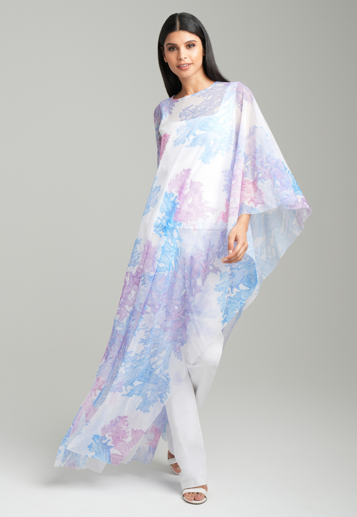 Woman wearing rainbow coral printed mesh one armed kaftan poncho over italian stretch cotton white tank top and pants by Ala von Auersperg for resort 2023