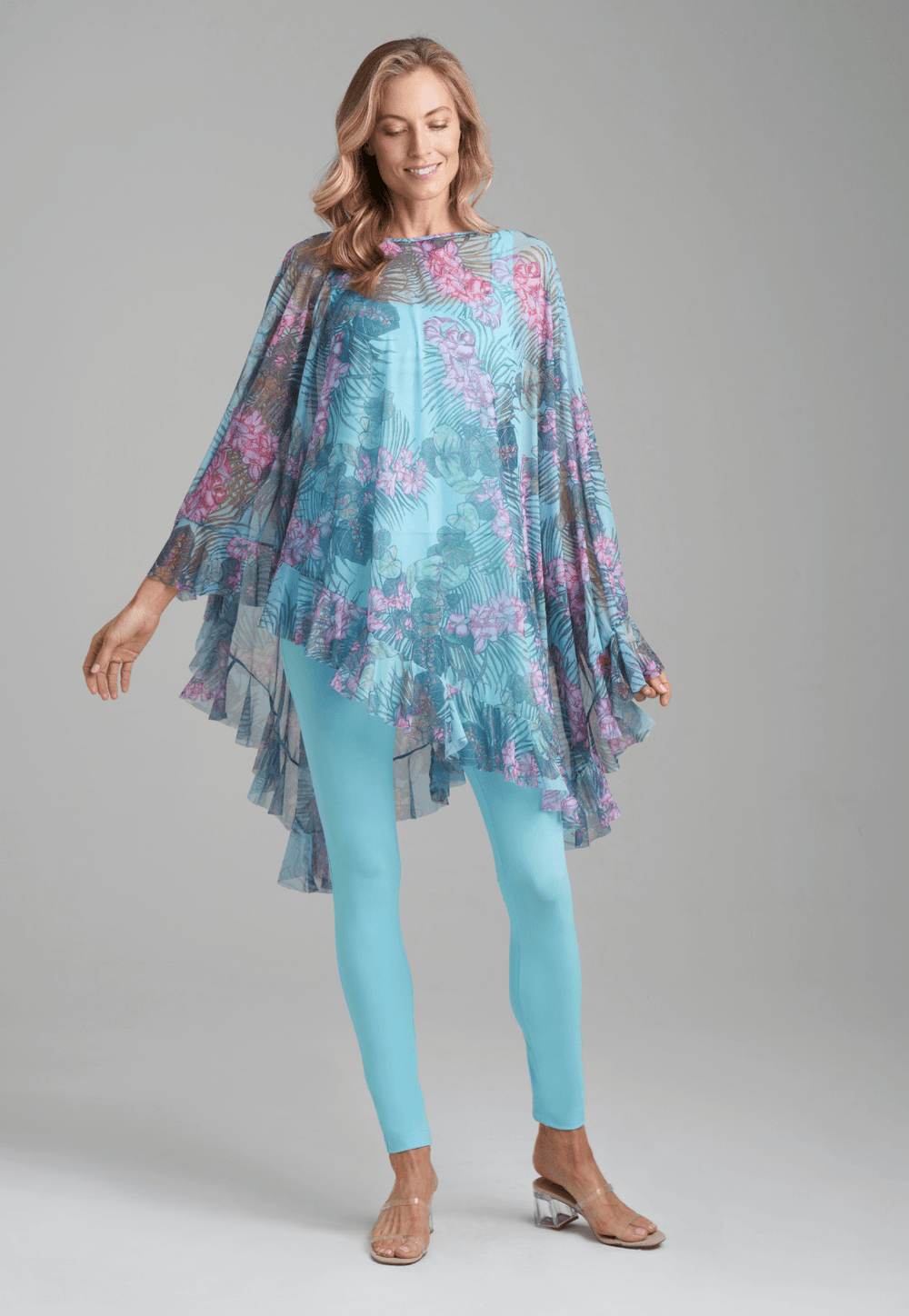 Woman wearing mesh printed orchid and palm poncho over stretch knit tank top and stretch knit pant in solid blue by Ala von Auersperg for resort 2022