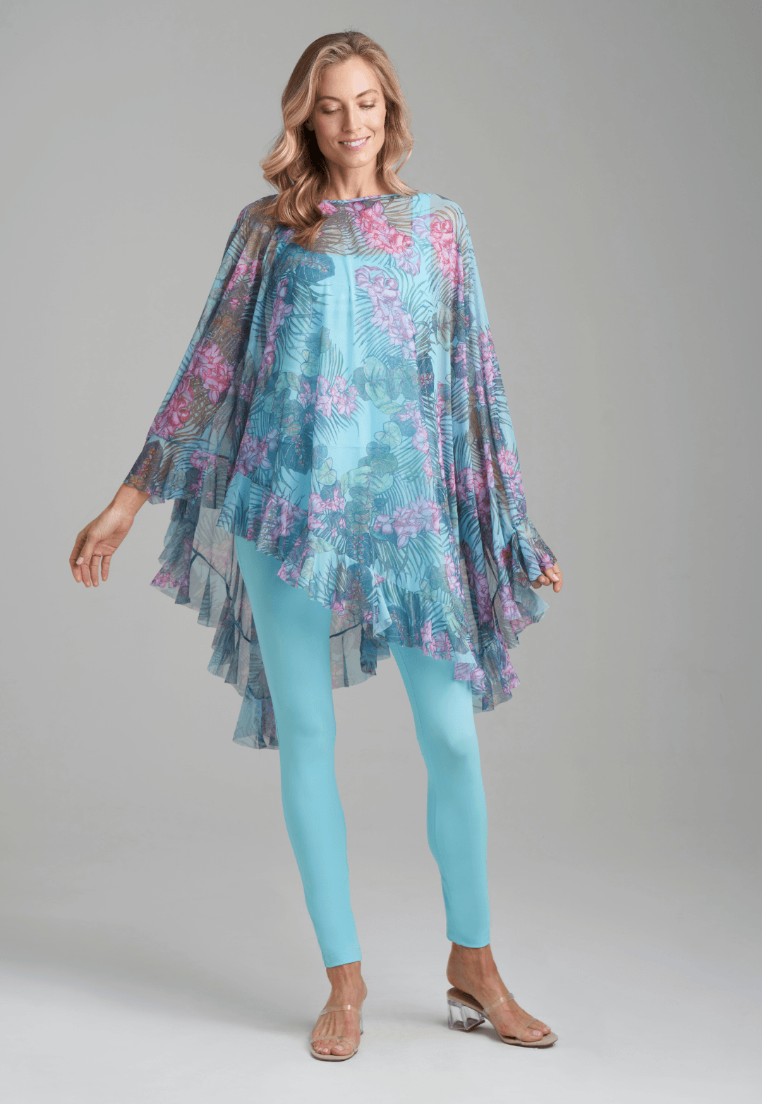 Woman wearing mesh printed orchid and palm poncho over stretch knit tank top and stretch knit pant in solid blue by Ala von Auersperg for resort 2022