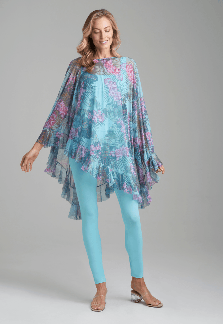 Woman wearing mesh printed orchid and palm poncho over stretch knit tank top and stretch knit pant in solid blue by Ala von Auersperg for resort 2022