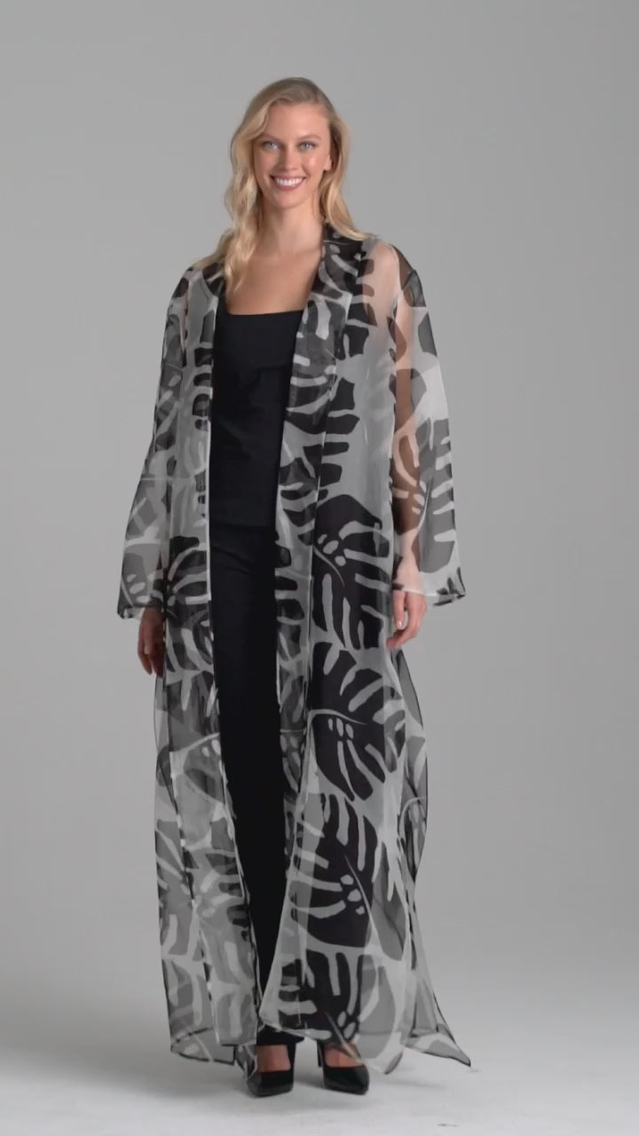 Woman wearing silk black and white palm leaf printed printed organza long jacket duster over italian stretch cotton square neck tank top and pant in black by Ala von Auersperg for holiday 2022