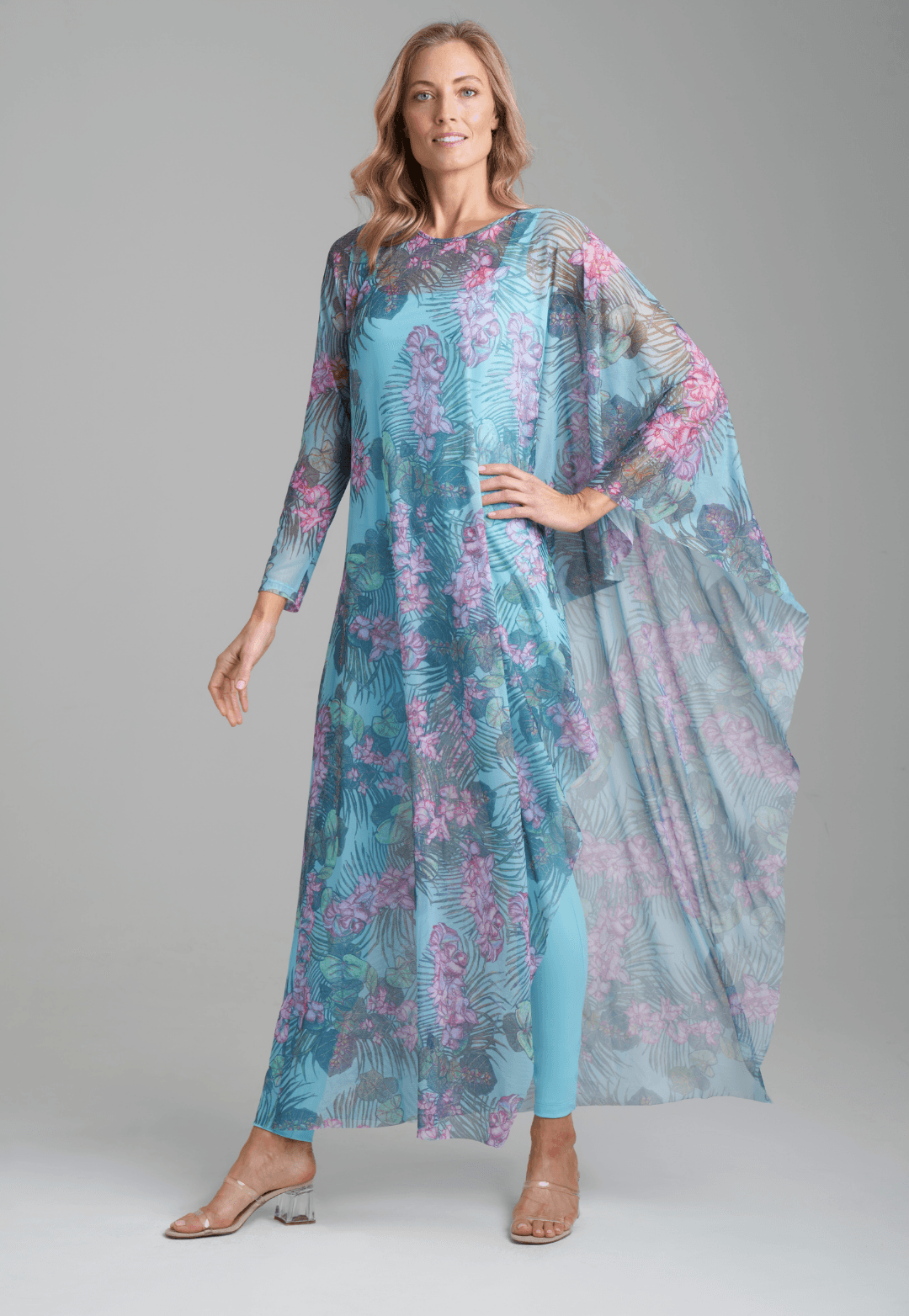 Woman wearing stretch knit solid blue green tank top with printed mesh orchid and palm one sleeve kaftan by Ala von Auersperg for resort 2022