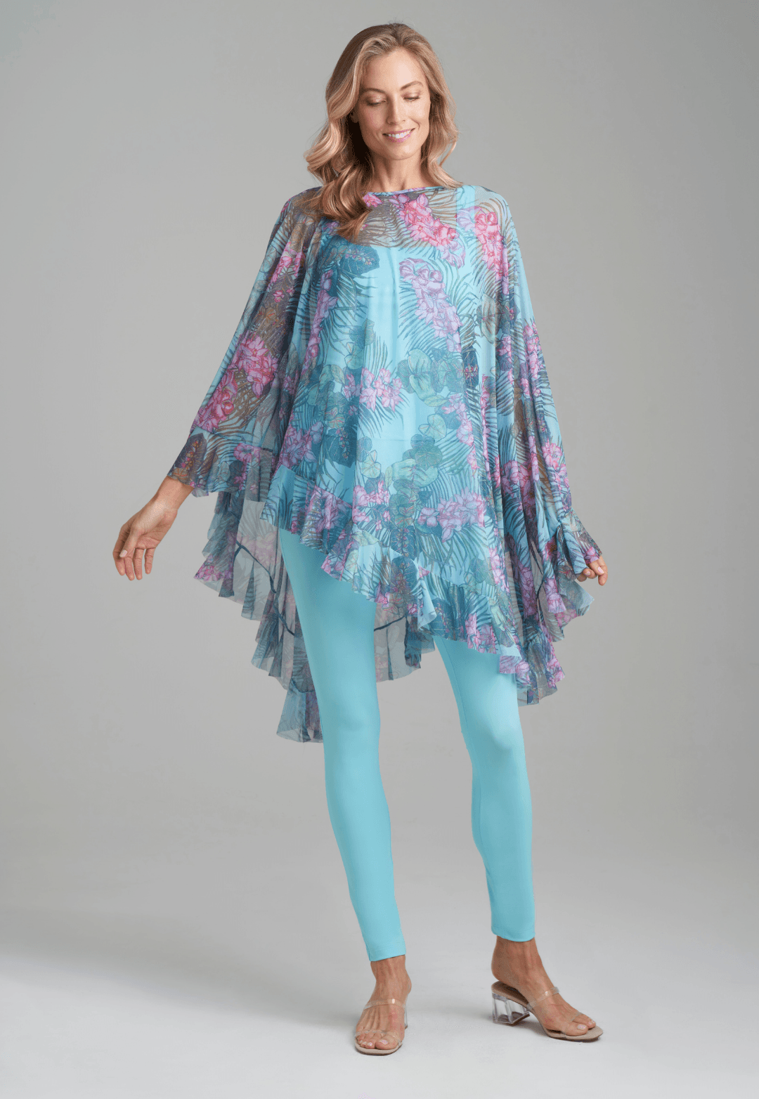 Woman wearing stretch knit tank top and pants in blue green with mesh poncho in printed orchid and palm over by Ala von Auersperg for resort 2022