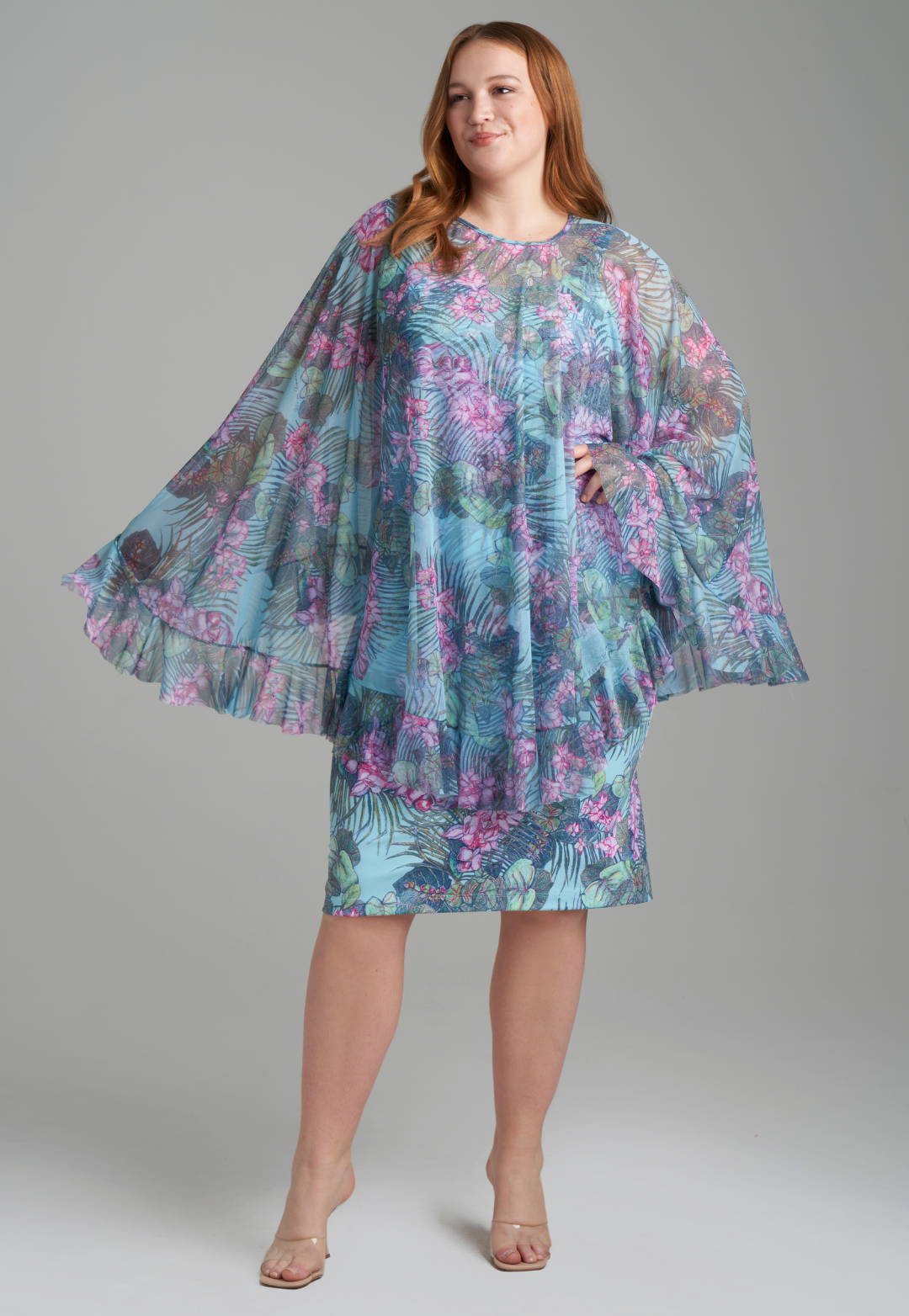 Woman wearing mesh printed orchid and palm poncho over a stretch knit short dress printed in orchid and palm by Ala von Auersperg for resort 2022
