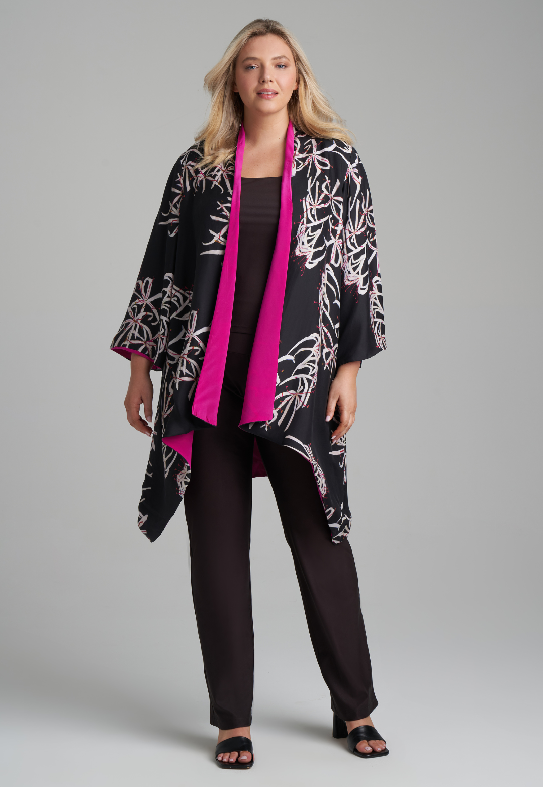 Woman wearing silk black spider lily printed reversible pink robe jacket over black stretch knit tank top and pant by Ala von Auersperg