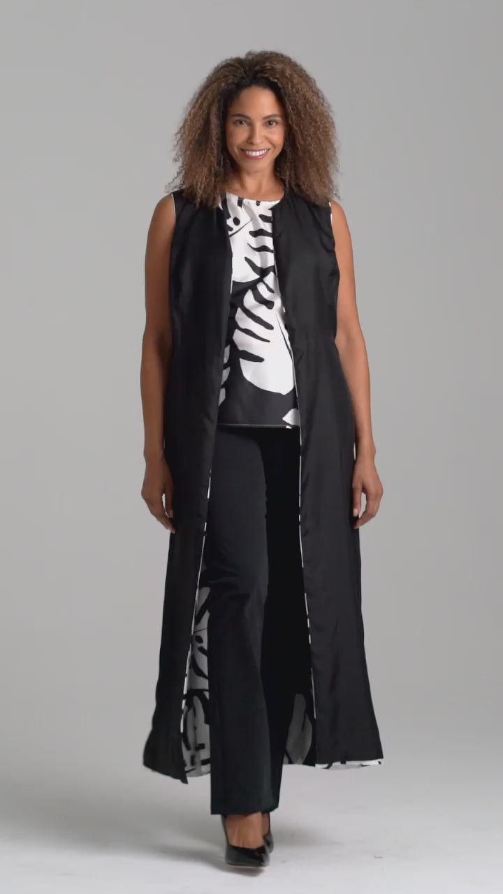 Woman wearing black and white palm leaf printed silk shell tank top with italian stretch cotton black pants and reversible silk palm leaf black and white printed long vest by Ala von Auersperg for holiday 2022
