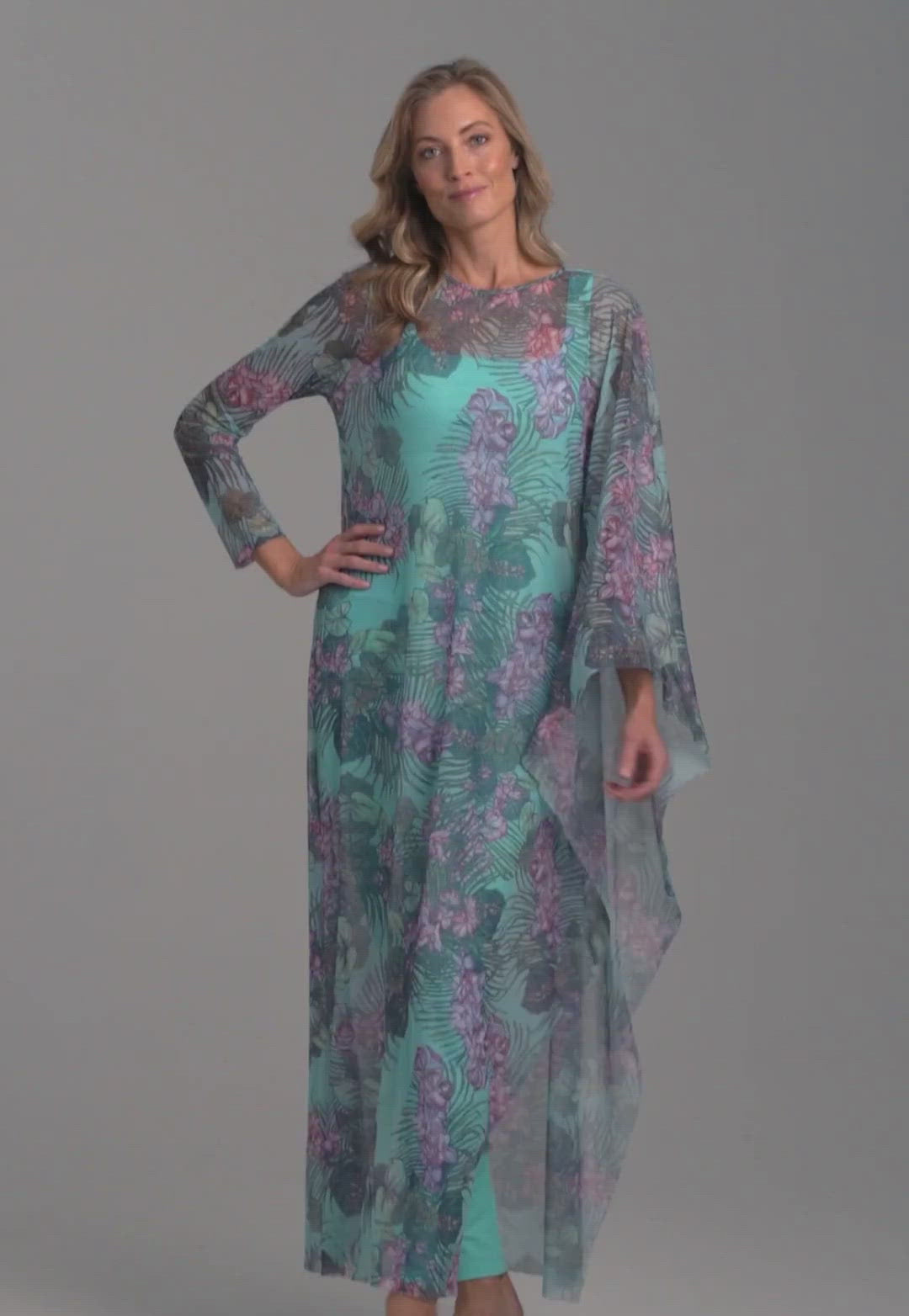 Woman wearing mesh long one sleeved poncho printed in orchid and palm over stretch knit long printed orchid and palm green dress