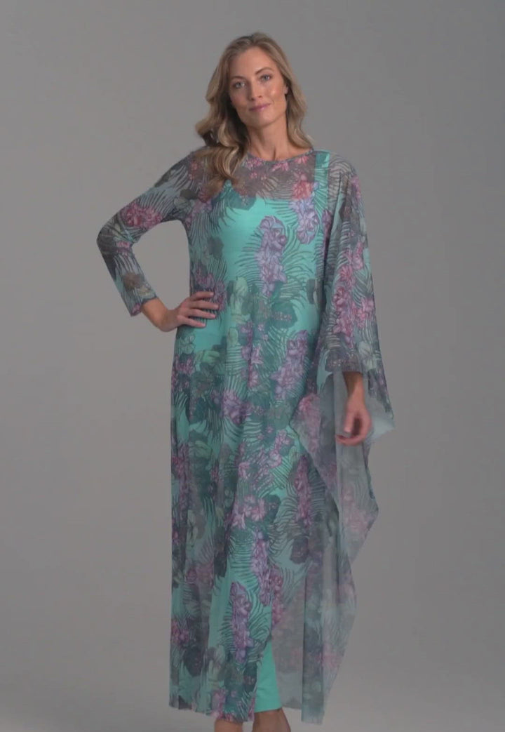 Woman wearing mesh long one sleeved poncho printed in orchid and palm over stretch knit long printed orchid and palm green dress